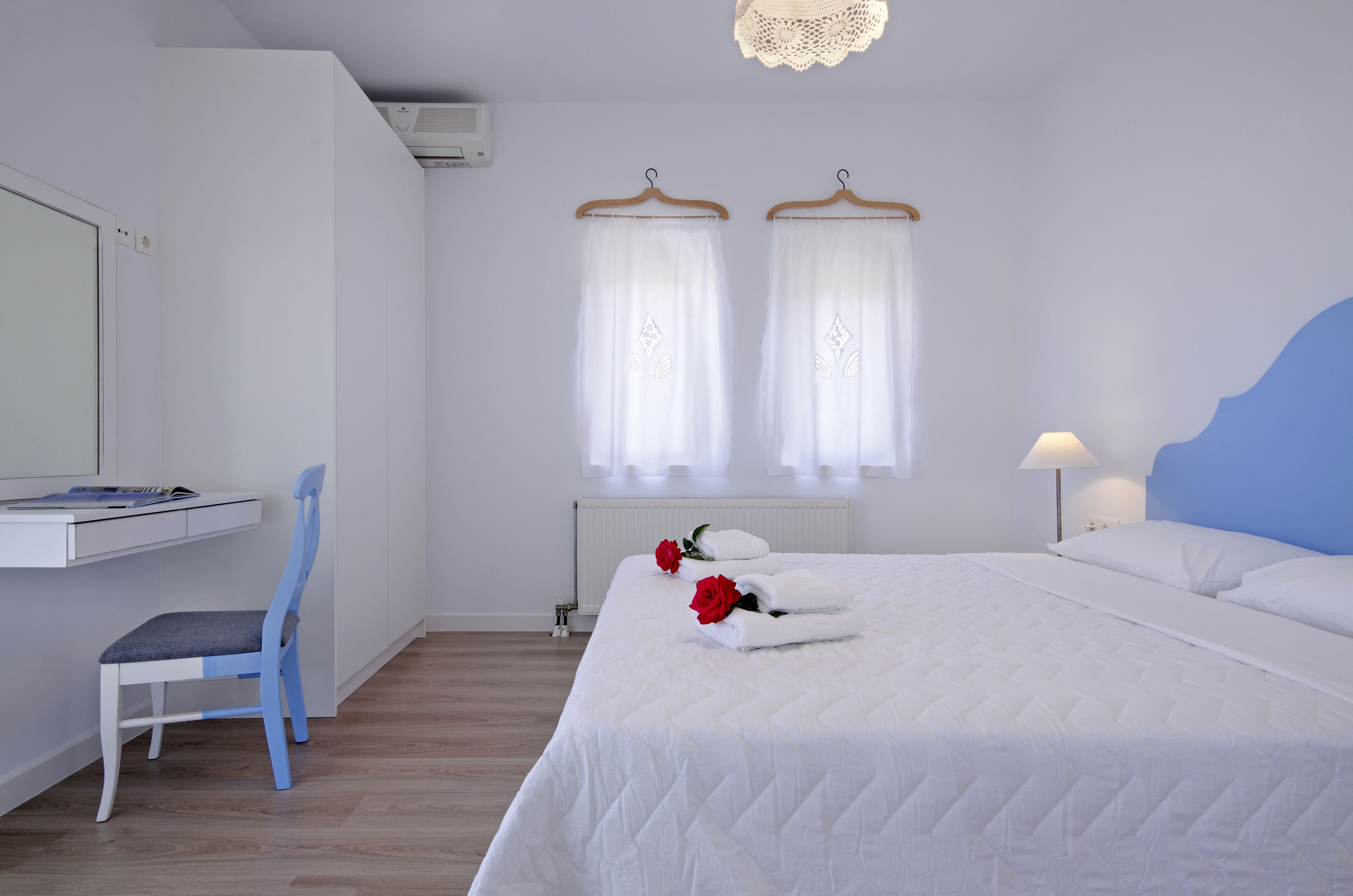A bedroom with a bed, a desk, a chair, and two windows with curtains.