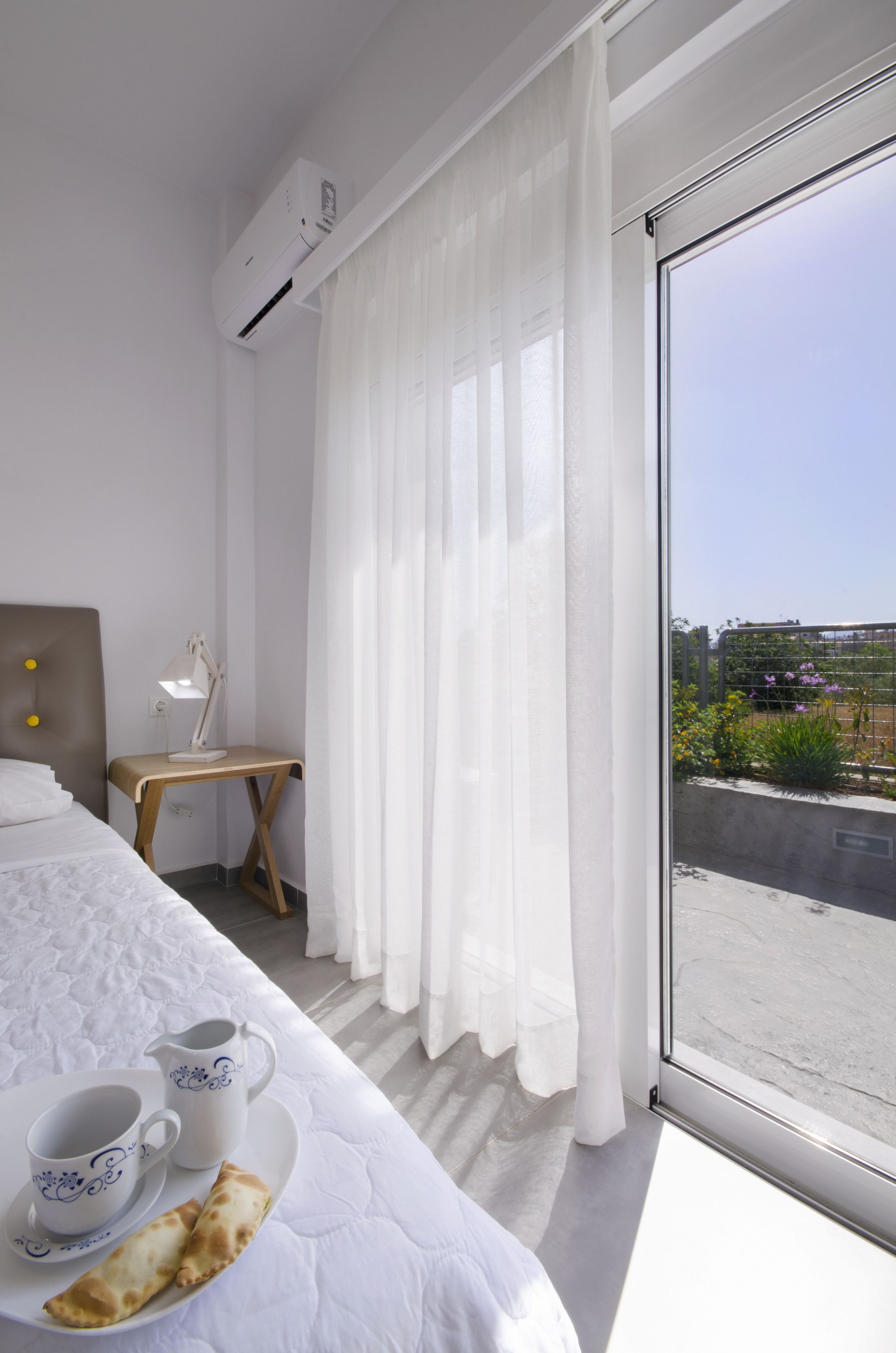 Ein Hotelzimmer mit Bett, Schreibtisch, einem Fenster mit Vorhängen und Blick nach draußen.