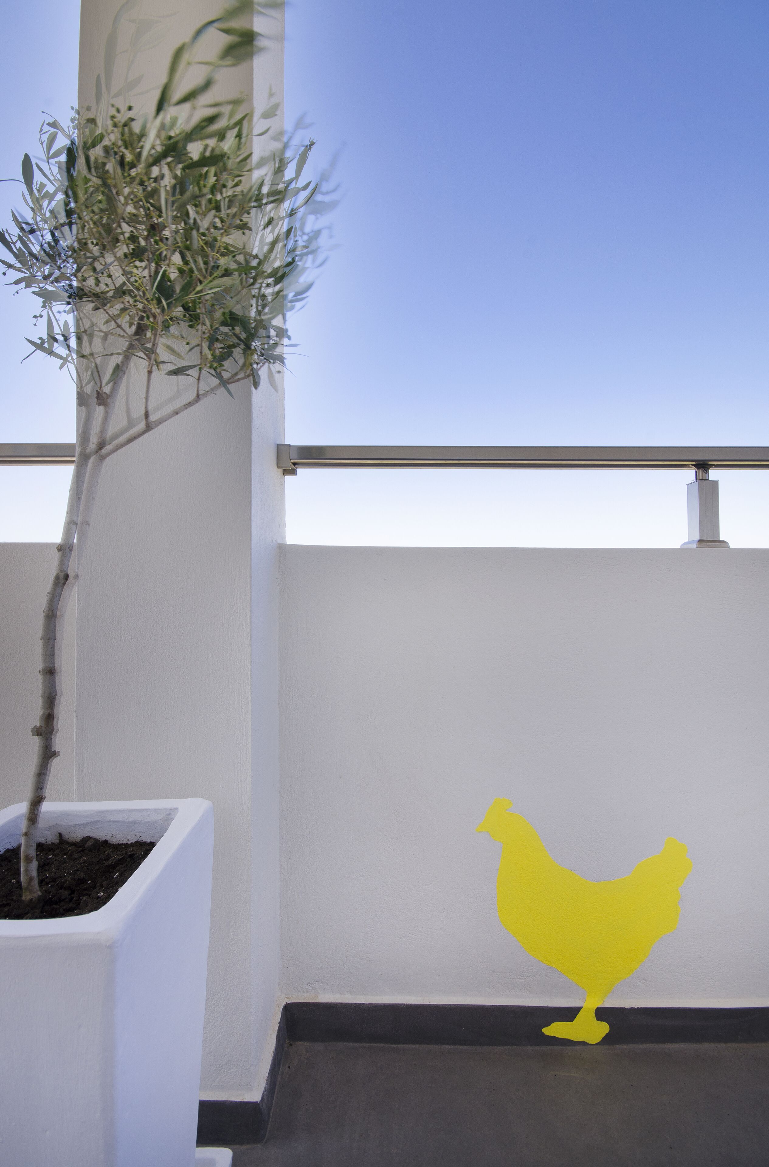Ein Balkon mit einem Blumentopf und einer gelben Silhouette eines Hühnchens an der Wand.