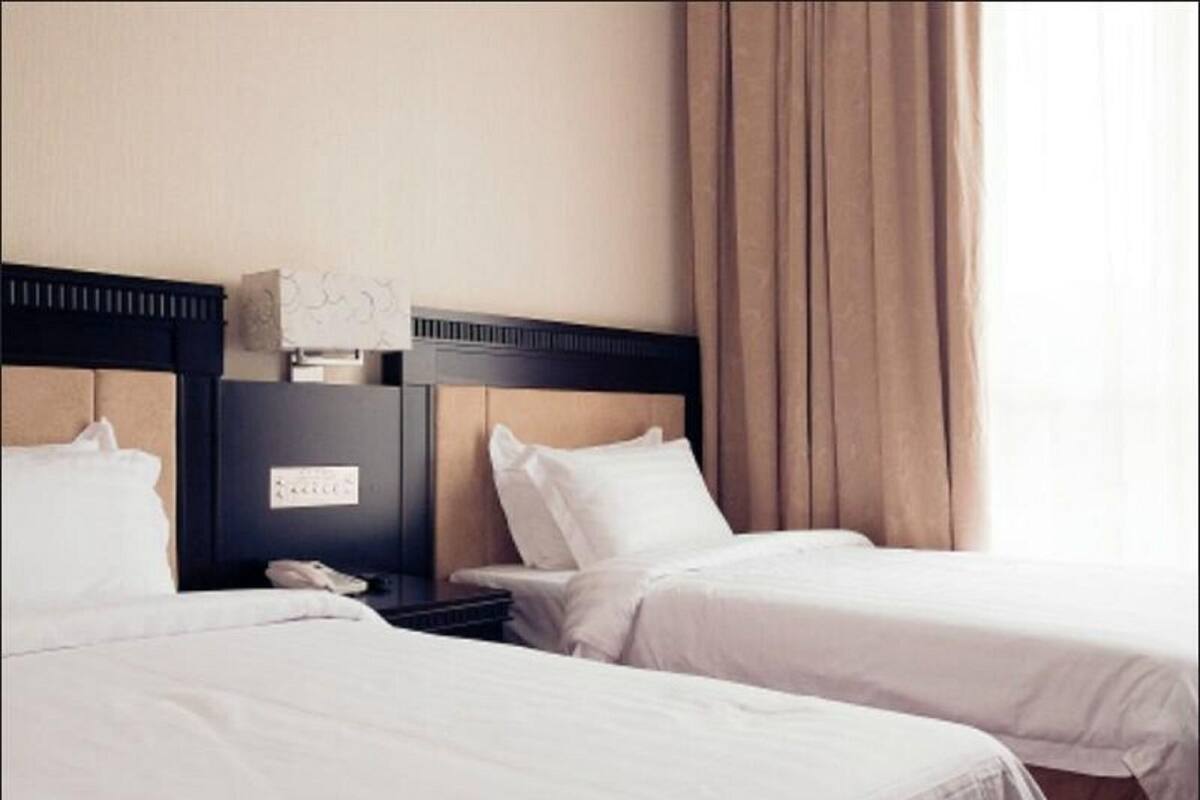Ein Hotelzimmer mit zwei Betten, einem Nachttisch und einem Fenster mit Vorhängen.