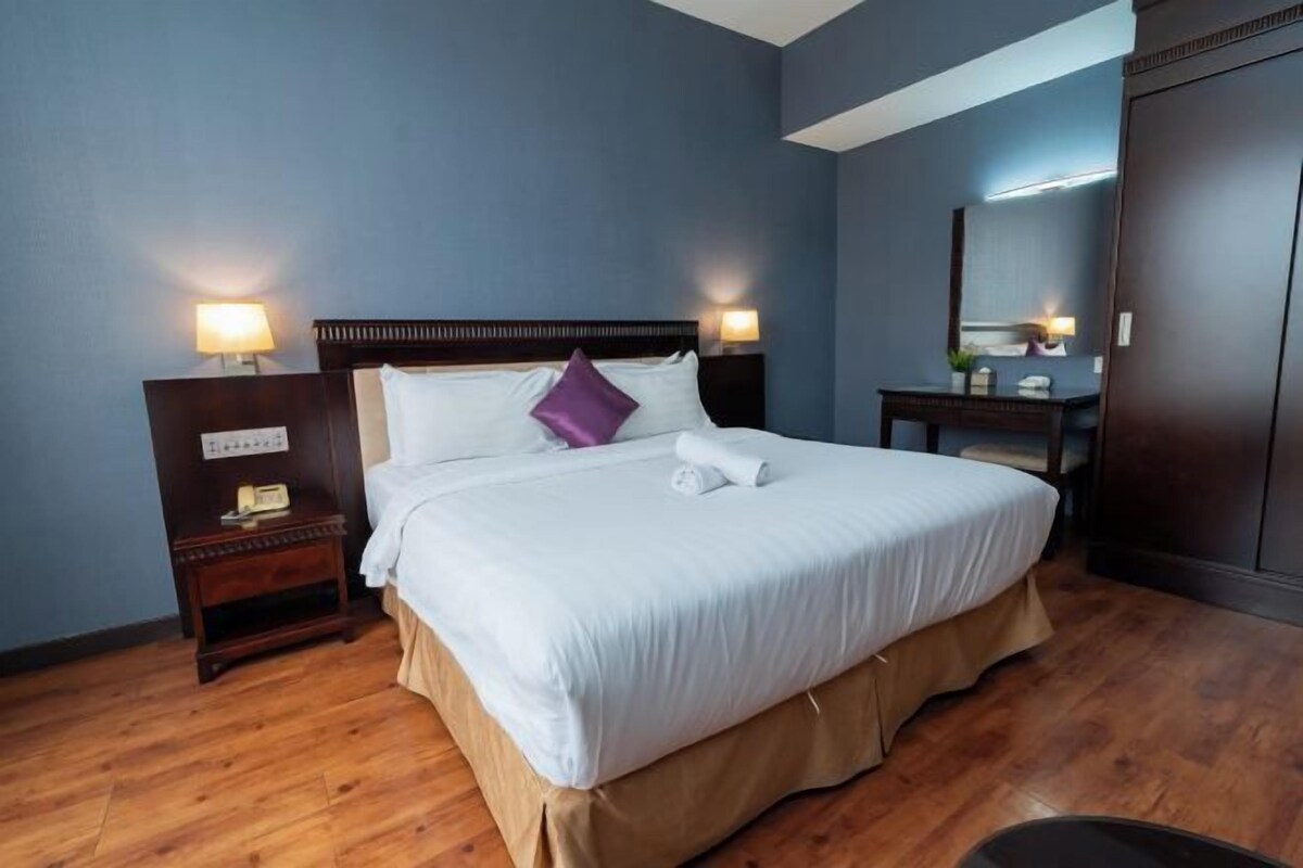 A hotel room with a large bed, bedside tables, a nightstand, a dresser, and a mirror.
