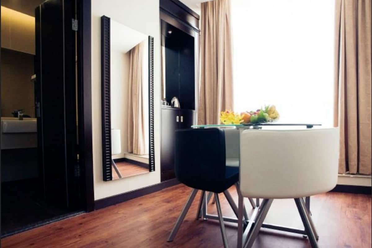 Ein Hotelzimmer mit Holzboden, einem Glastisch mit Obstschale, einem schwarz-weißen Stuhl, einem Spiegel und einem Kleiderschrank.