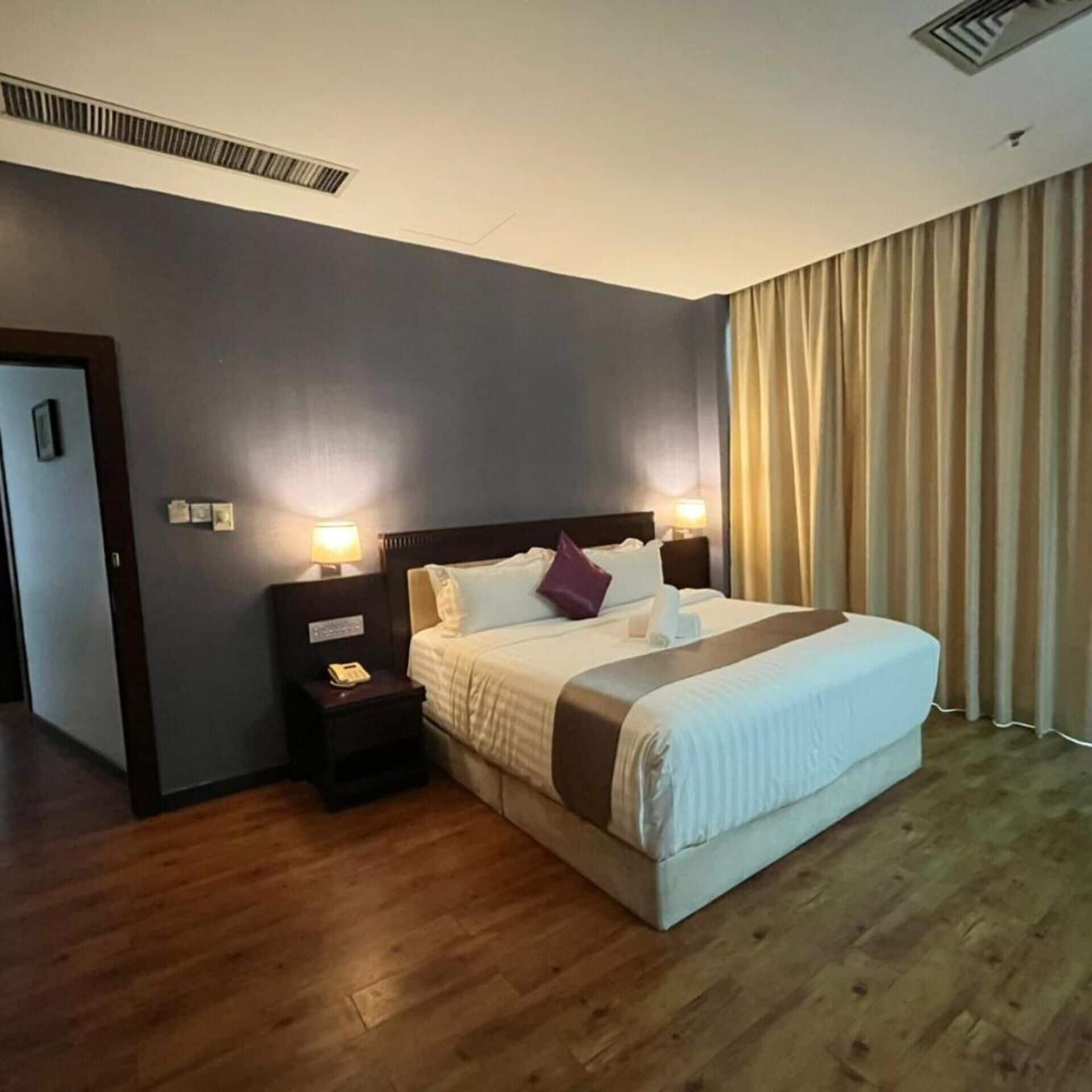 A hotel room with a large bed, two bedside tables, a wall-mounted heater, and a door.