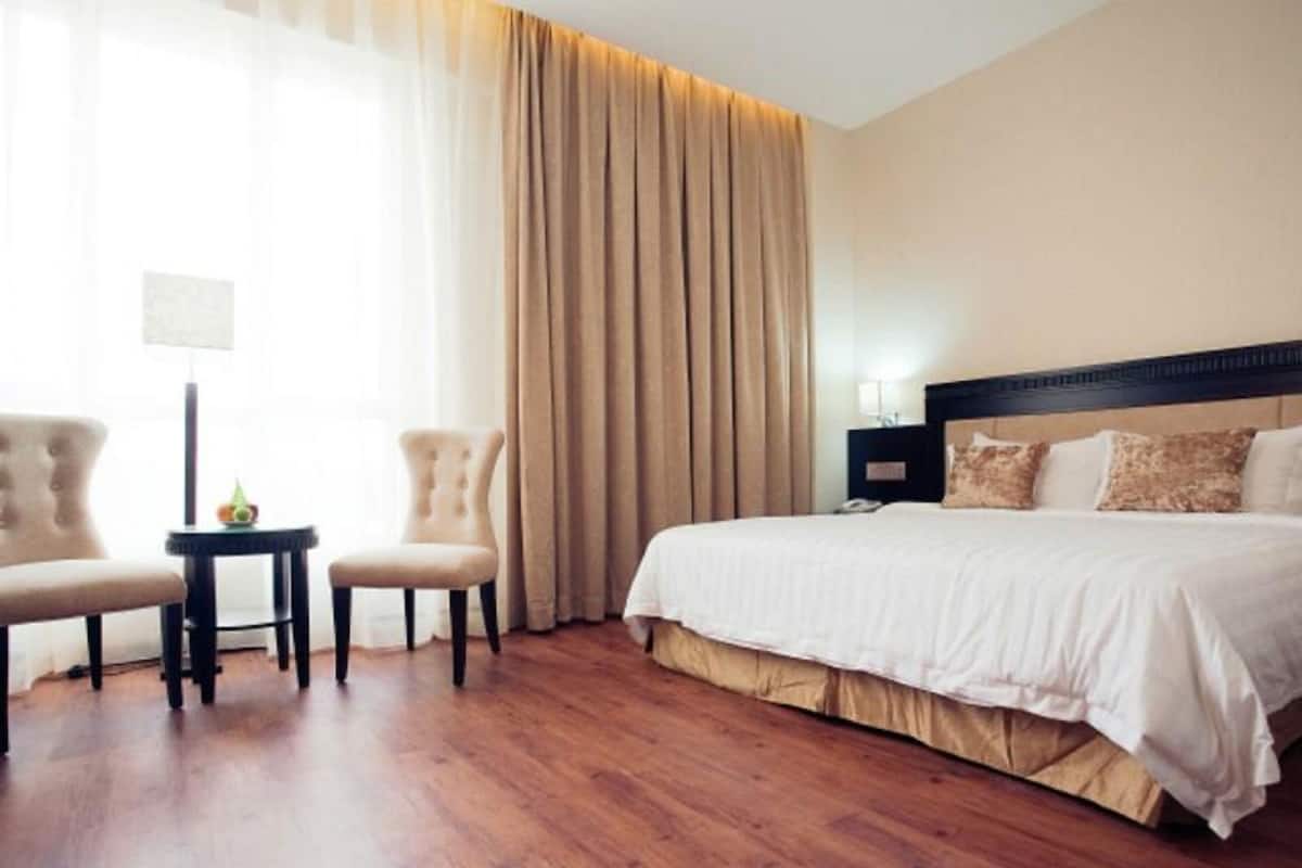 Ein Hotelzimmer mit einem großen Bett, zwei Sesseln, einem kleinen Tisch und einem Nachttisch.