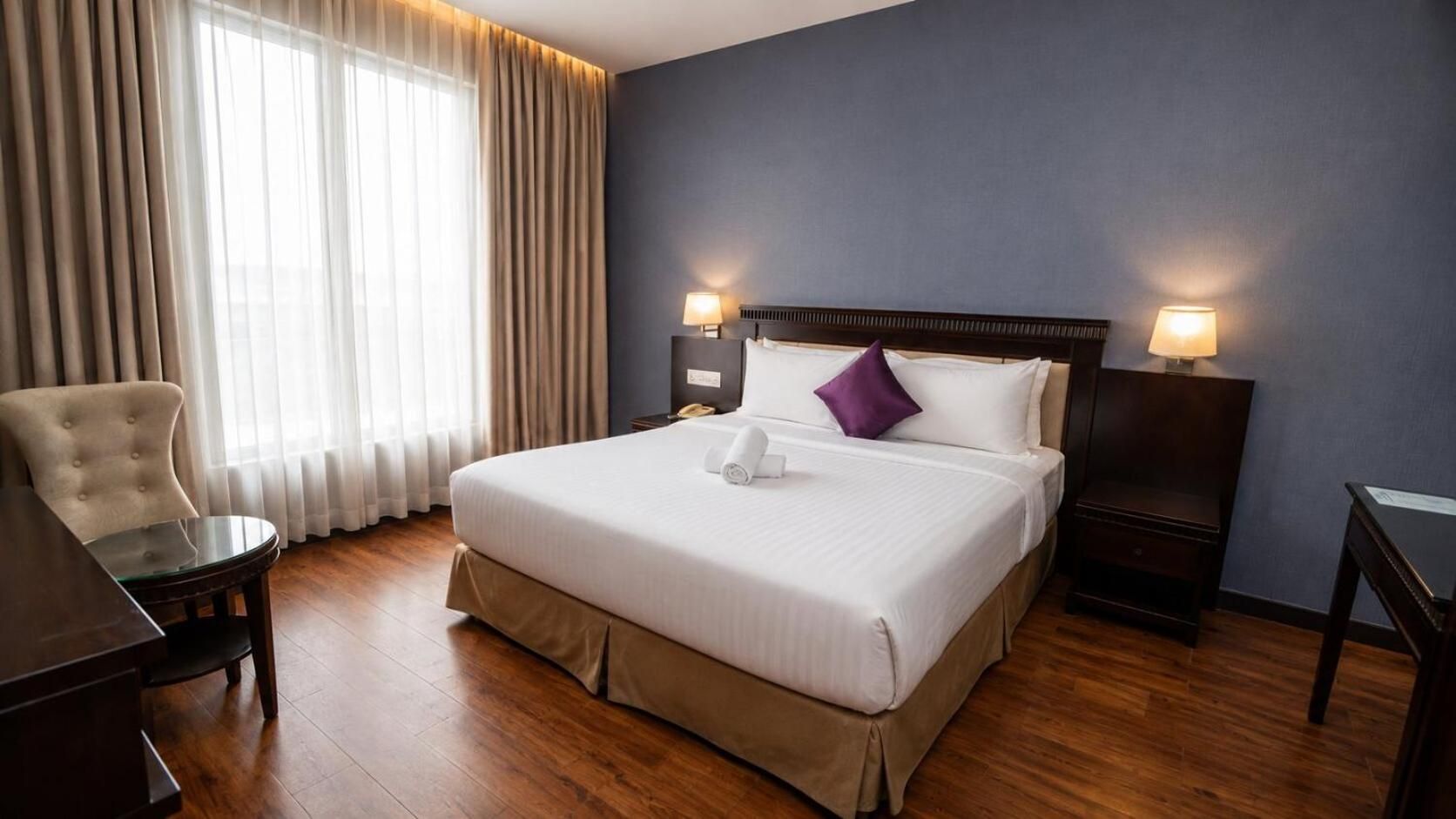 A hotel room with a large bed, two bedside lamps, a chair, and a desk.