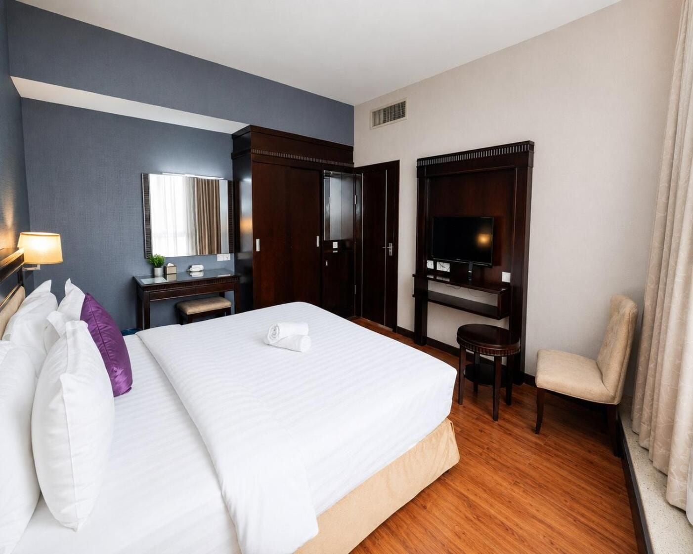 A hotel room with a large bed, a desk with a chair, a television, and a window with curtains.