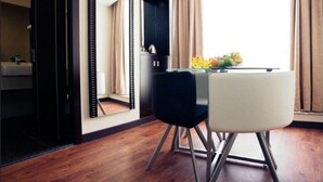 Habitació d'hotel amb terra de fusta, taula de dinar amb cadires, un mirall i una finestra amb cortines.
