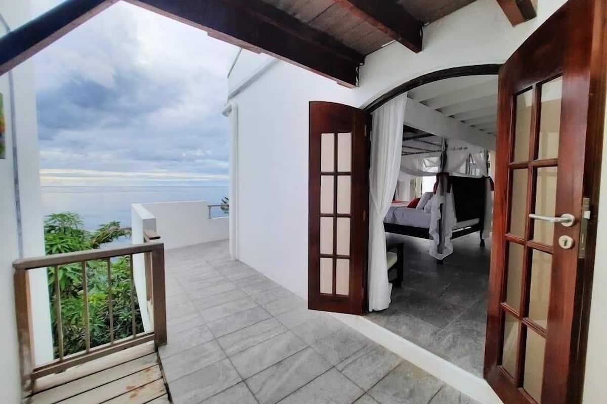 Een balkon met uitzicht op zee, een bed met hemelbed en een houten deur.