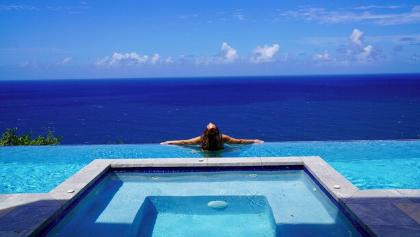 Une personne se détend dans une piscine avec vue sur l’océan.