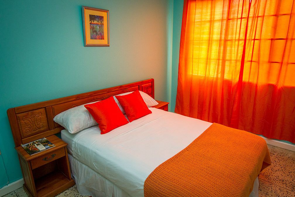 A neatly made bed with white and red bedding, a wooden headboard, and a nightstand with a magazine.