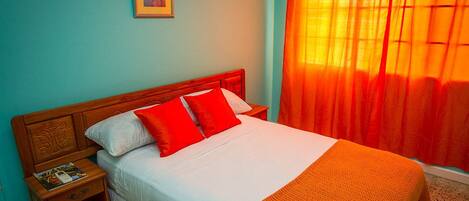 A neatly made bed with white and red bedding, a wooden headboard, and a nightstand with a magazine.