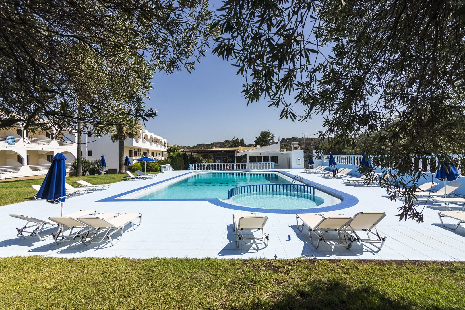 A swimming pool with lounge chairs and umbrellas, surrounded by buildings and trees.