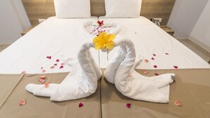 Een keurig opgemaakt bed met witte lakens, een houten hoofdbord en een decoratieve zwaan van handdoeken met een gele bloem.