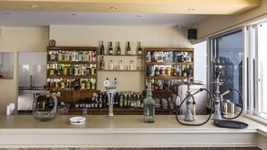 Een bar met schappen vol drankflessen, een grote glazen vaas en een waterpijp op de bar.