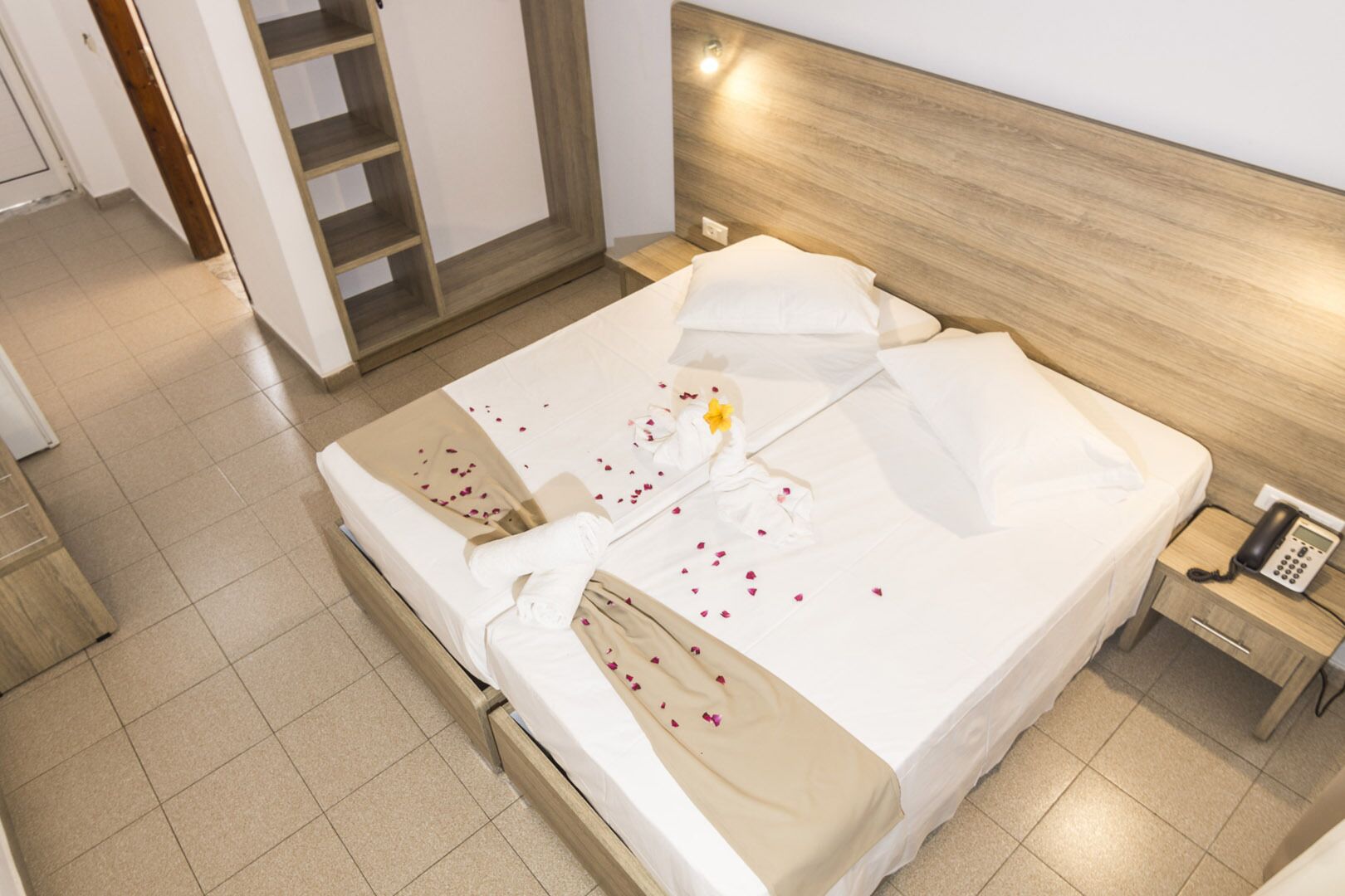 Een keurig opgemaakt bed met witte lakens, een houten hoofdbord en een telefoon op het nachtkastje.