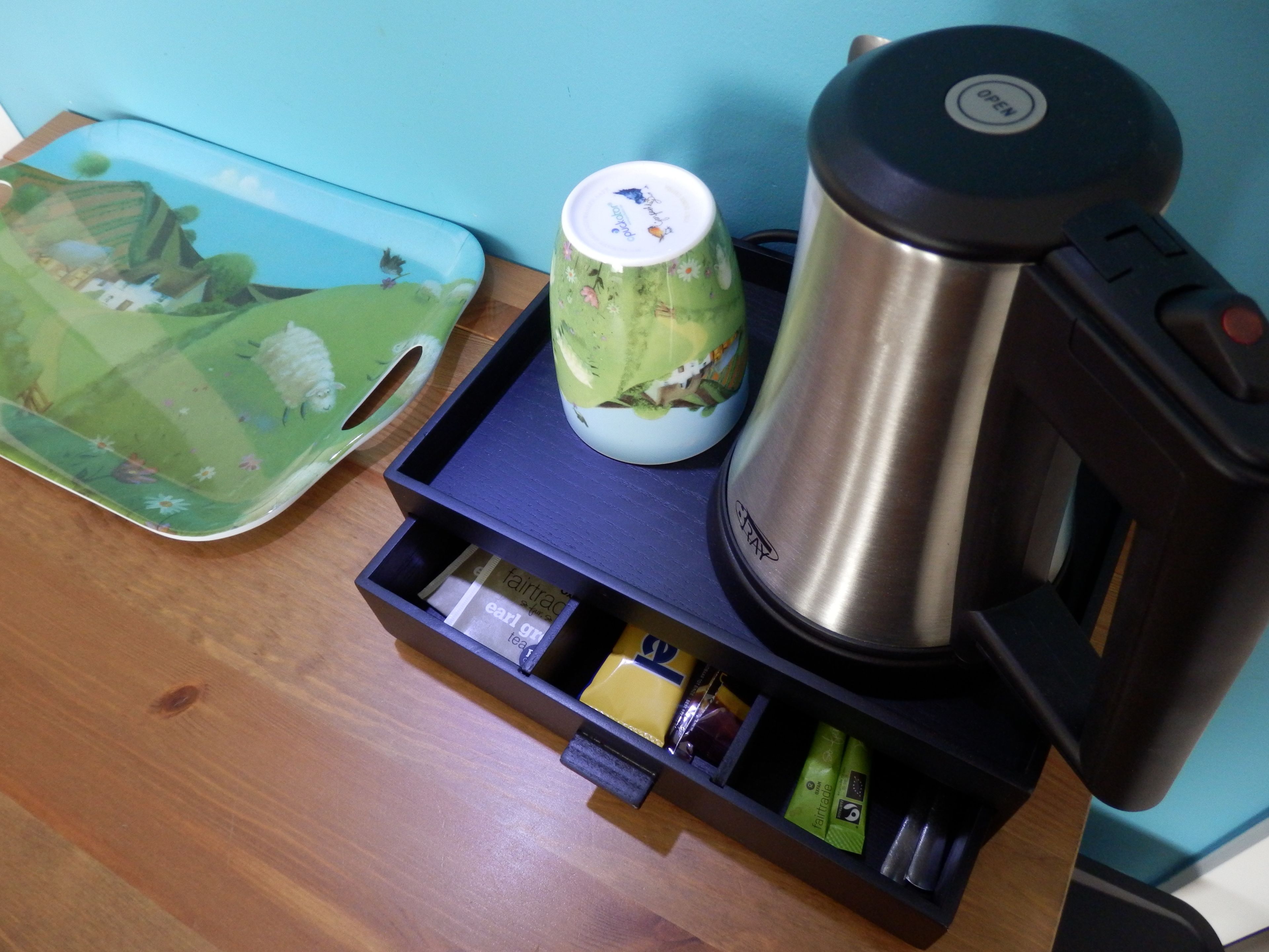 A kitchen counter with a coffee maker, a mug, and a tray with a teapot and tea bags.