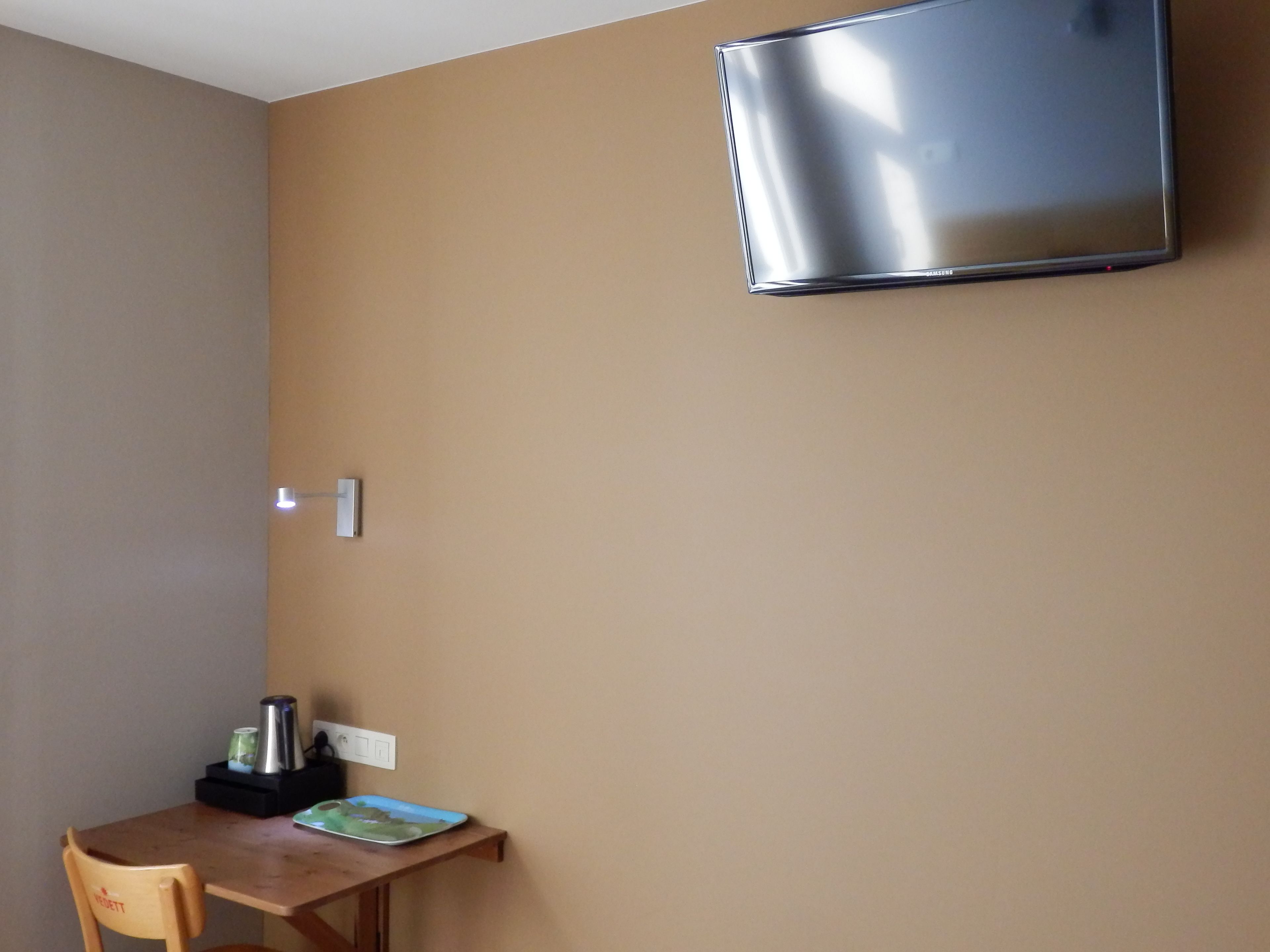 Une petite pièce avec une table en bois, une chaise, une bouilloire et un téléviseur à écran plat fixé au mur.