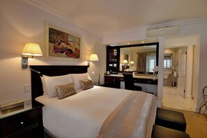 A hotel room with a large bed, two bedside lamps, a painting on the wall, a desk with a mirror, and a bathroom visible through an open door. - The Coach House at Val du Charron (Wellington)