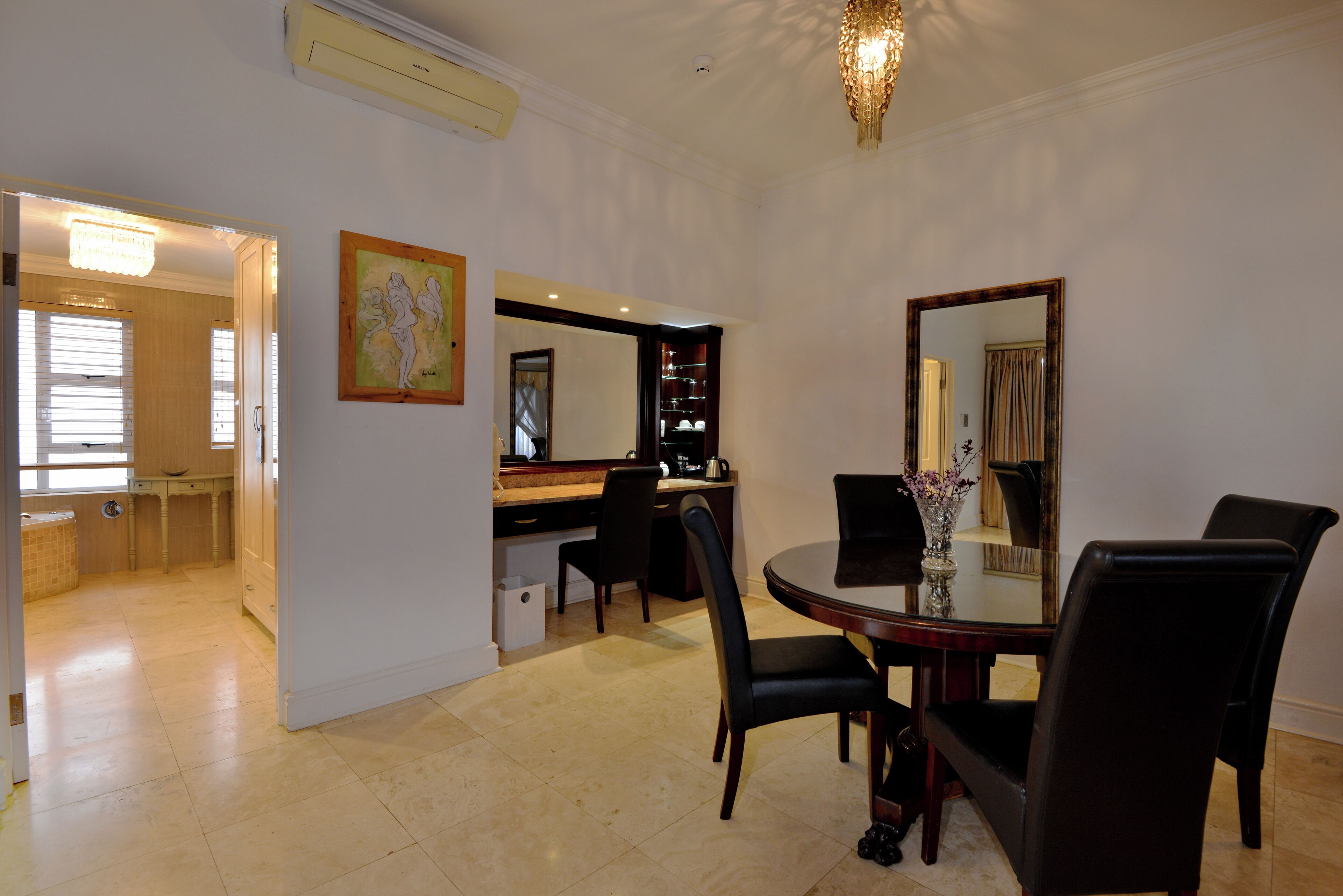 A dining area with a round table, black chairs, a vase with flowers, and a mirror on the wall.