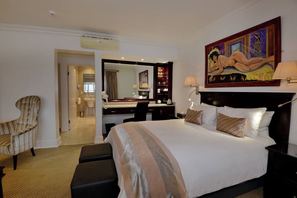 Quarto de hotel com uma cama grande, uma escrivaninha, uma cadeira e um banheiro visível por uma porta aberta.