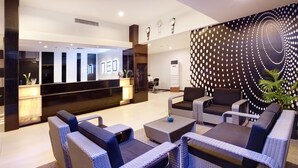 A modern lobby with a reception desk, wicker furniture, and a decorative wall. - Hotel Neo Palma - Palangkaraya by ASTON (Palangkaraya)