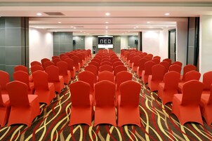 A hotel conference room with rows of red chairs and a carpeted floor.