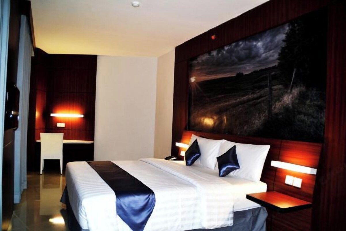 A hotel room with a large bed, bedside tables, a desk, and a painting on the wall.