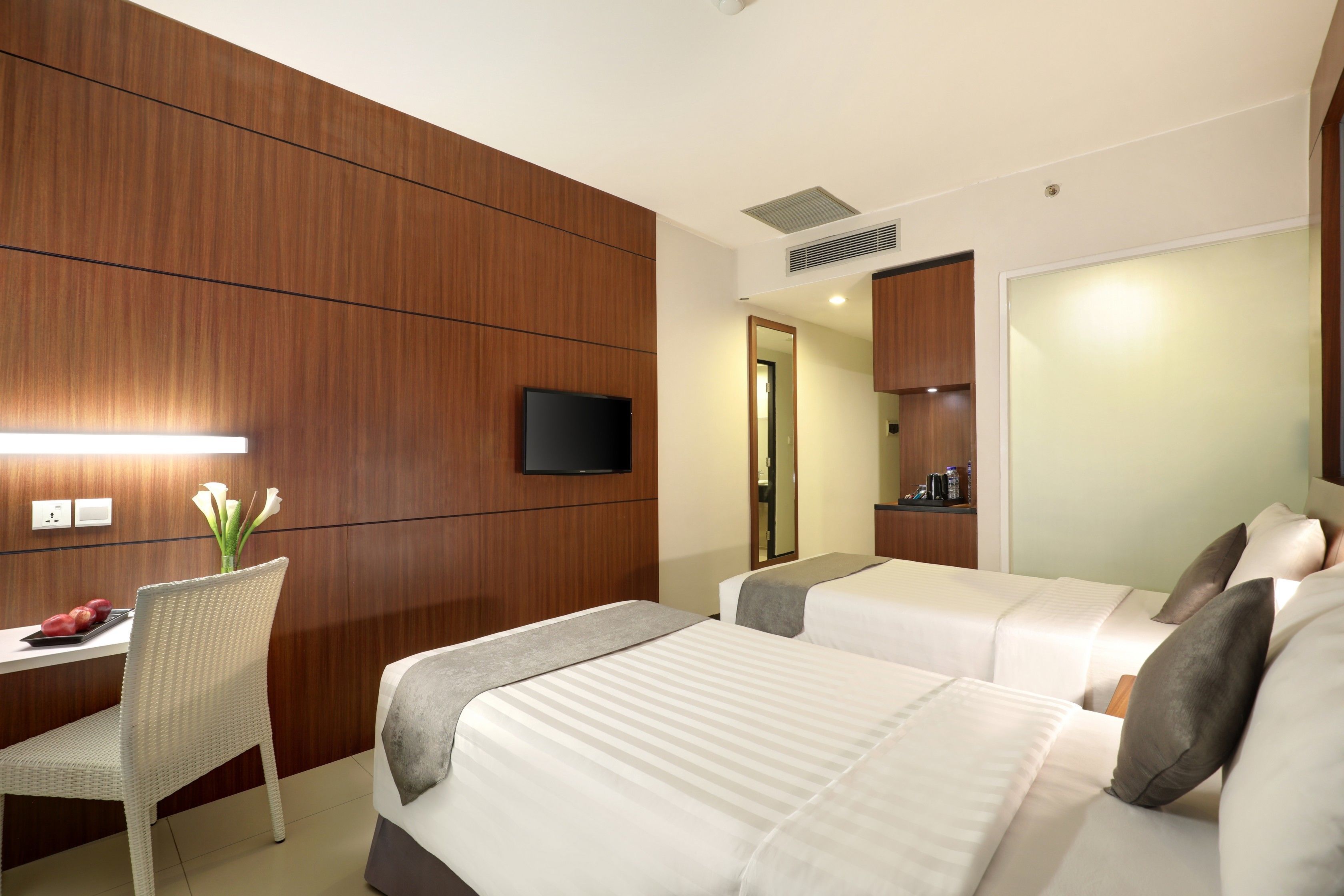 A hotel room with two beds, a desk, a chair, a TV, and a mirror.