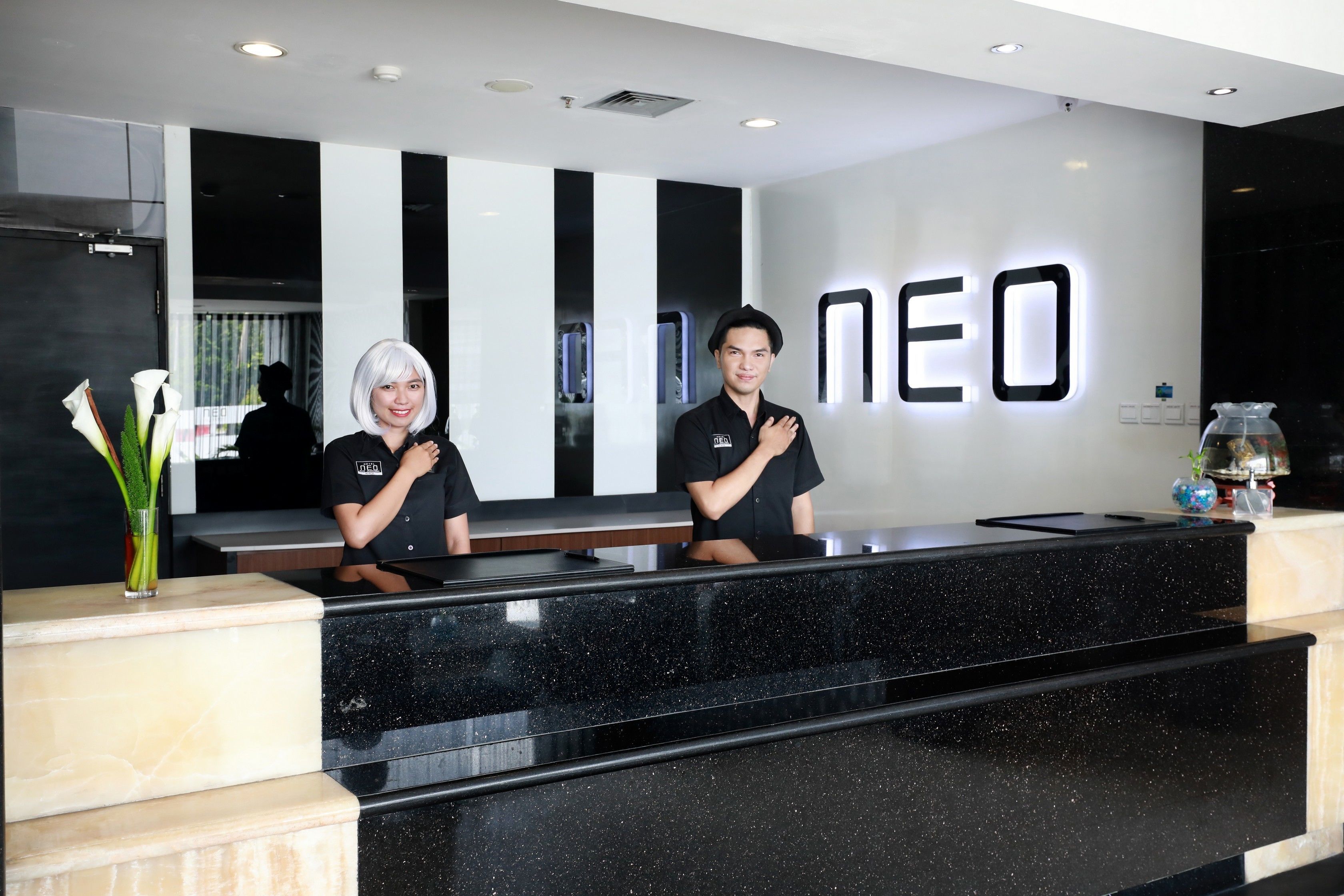 Un mostrador de recepción con cubierta de mármol negro y una pared blanca con las letras "NEO" iluminadas.
