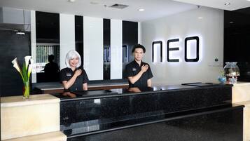Un mostrador de recepción con cubierta de mármol negro y una pared blanca con las letras "NEO" iluminadas.