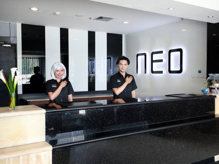 Un mostrador de recepción con cubierta de mármol negro y una pared blanca con las letras "NEO" iluminadas.