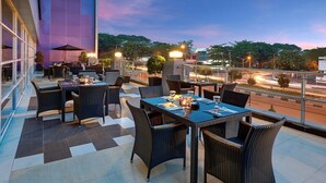 An outdoor dining area with tables and chairs, a view of the street, and a building in the background. - Hotel Neo Palma - Palangkaraya by ASTON (Palangkaraya)