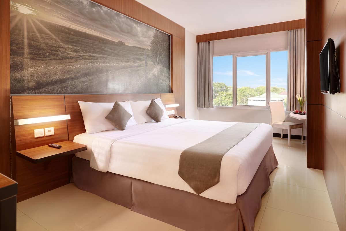 Ein modernes Hotelzimmer mit einem großen Bett, einem Flachbildfernseher, einem Schreibtisch und Blick ins Freie.