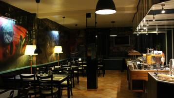 Un restaurante con un mural en la pared, mesas, sillas y una zona de bar con una máquina de café.