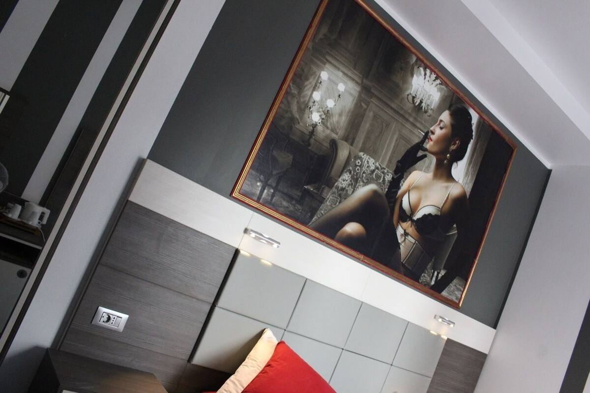 A modern hotel room with a large framed picture on the wall, a red accent pillow, and a built-in TV.