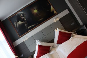 Ein modernes Hotelzimmer mit einem großen Bett, roter und weißer Bettwäsche, einem an der Wand befestigten Fernseher und einem dunkel gefärbten Kopfteil.
