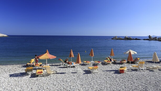 A beach with pebbles, umbrellas, and lounge chairs.