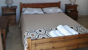 A neatly arranged bedroom with a wooden bed, two bedside tables with lamps, a wall-mounted light switch, and a painting of white tulips.