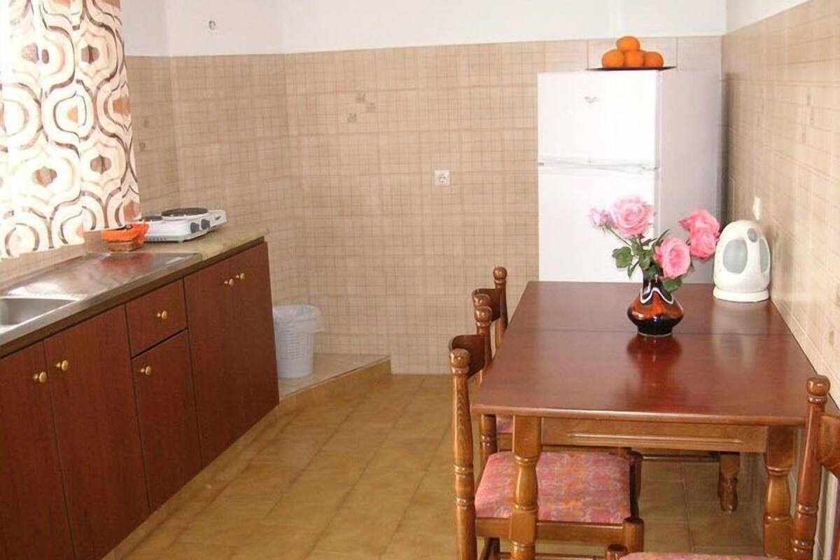 A kitchen with a wooden table, chairs, a refrigerator, and a sink.