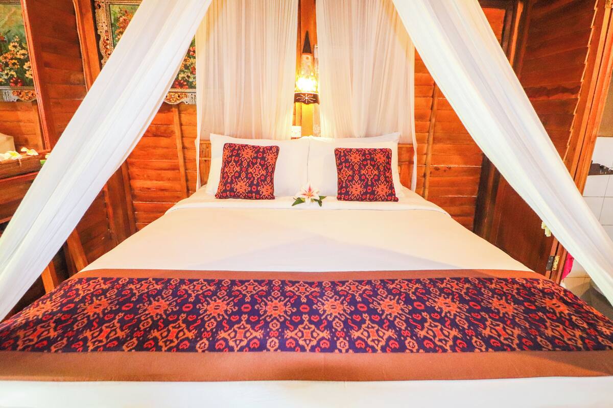 A bed with a canopy, two patterned pillows, and a floral arrangement.