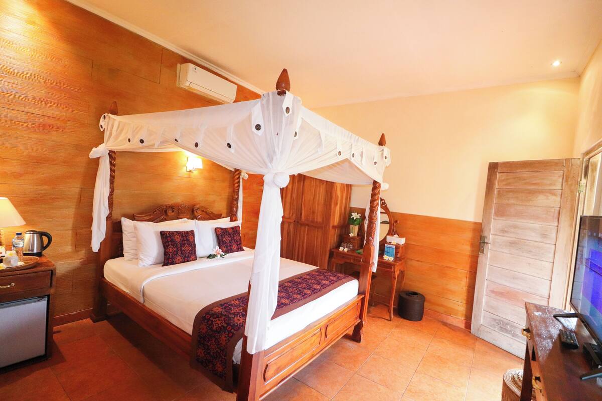 A four-poster canopy bed with a wooden headboard, a bedside table with a lamp, and a television on a wooden stand.