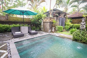 A pool area with lounge chairs and an umbrella, surrounded by greenery and stone structures. - Villa JJ and Spa Ubud (Ubud)