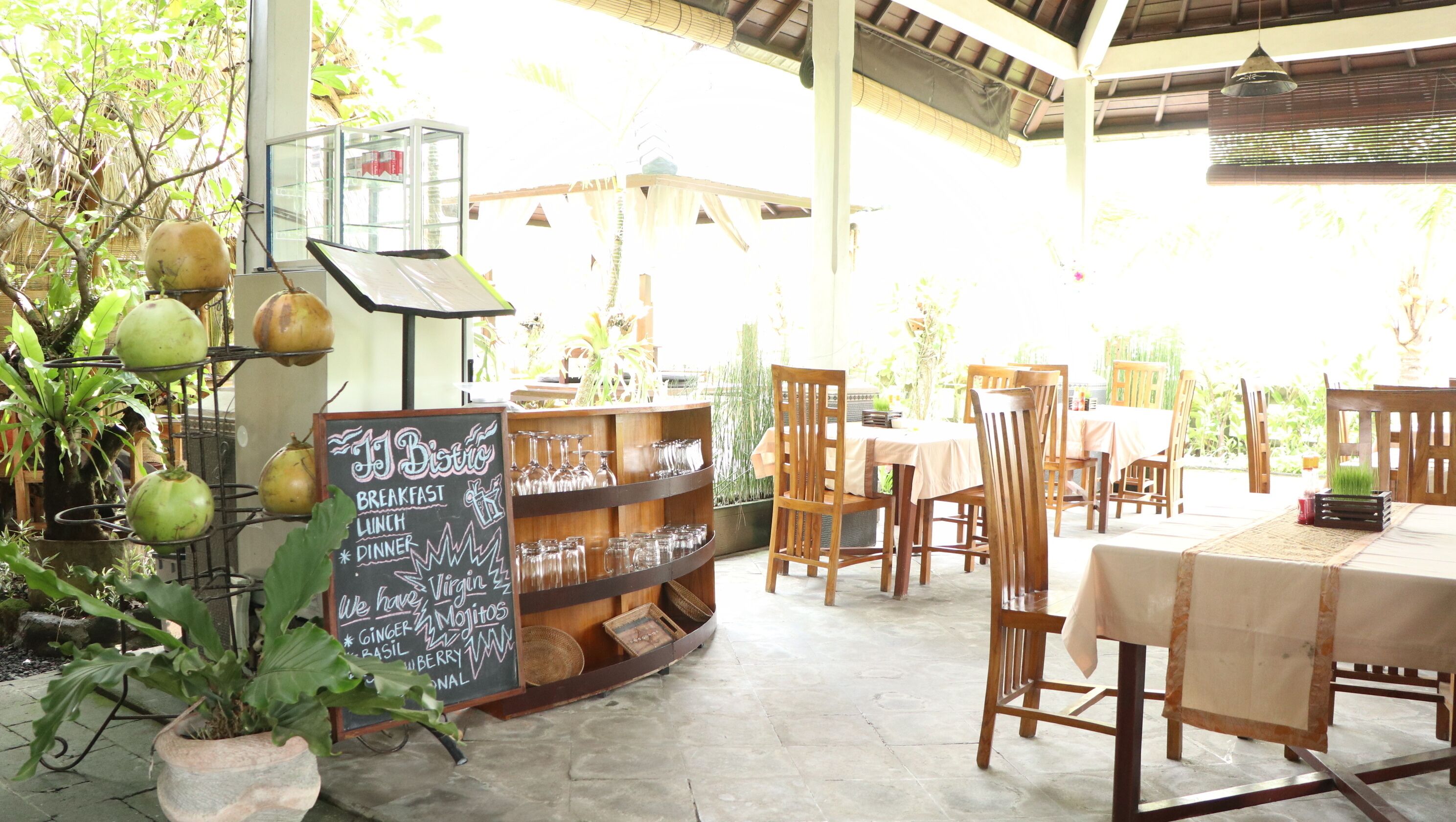 An outdoor cafe with wooden tables and chairs, a chalkboard menu, and potted plants.