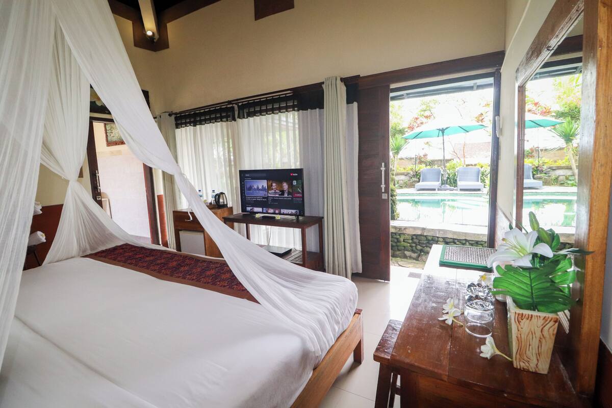 A bedroom with a bed, a TV, and a view of an outdoor pool area.