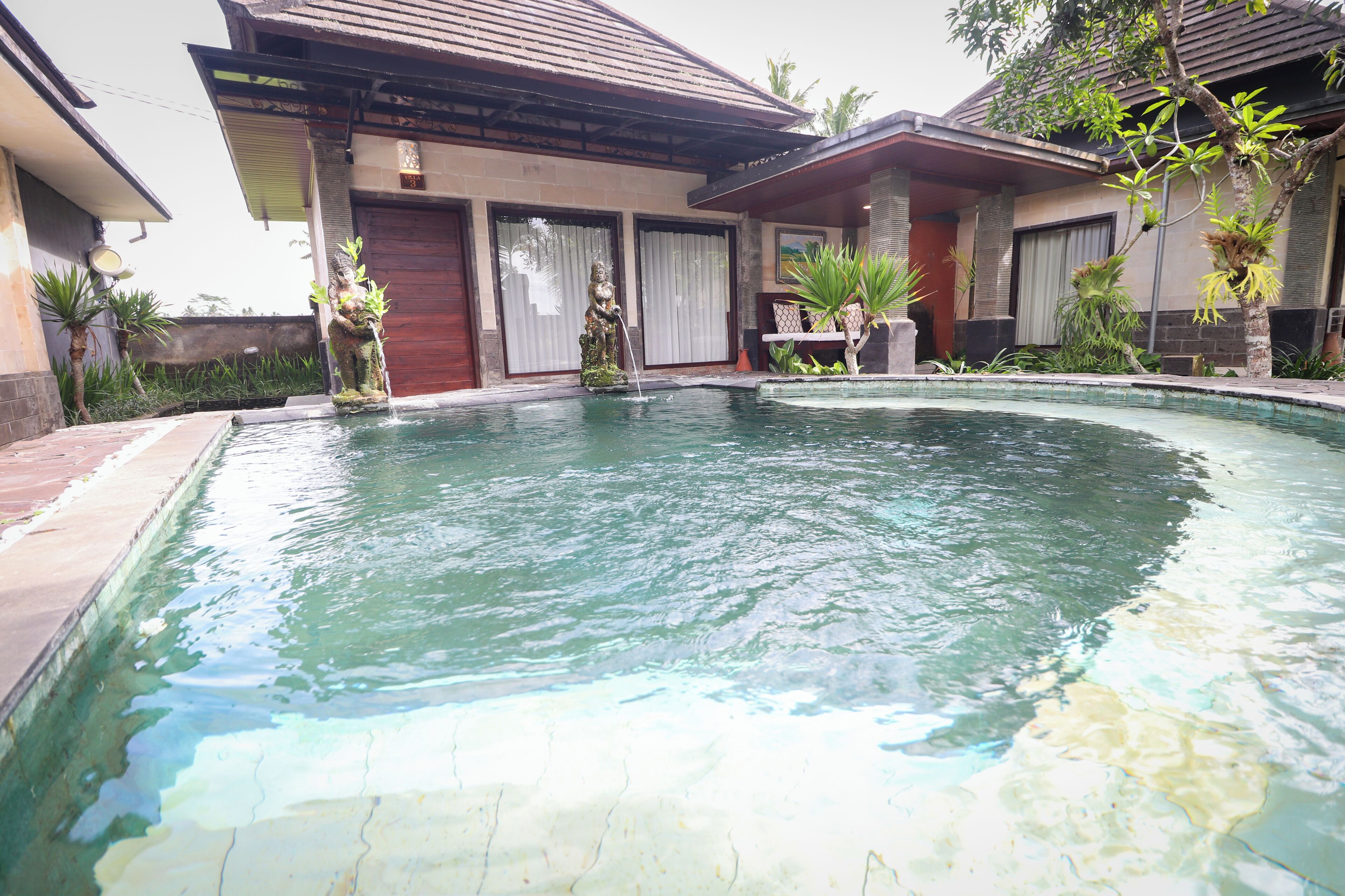 A swimming pool surrounded by a house with a tiled roof and a covered patio area.