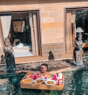 A person relaxing by a pool with a tray of food and drinks. - Villa JJ and Spa Ubud (Ubud)