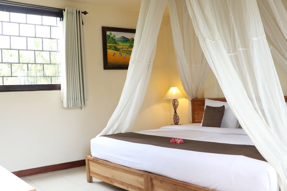 A bed with a canopy, a bedside lamp, and a painting on the wall.
