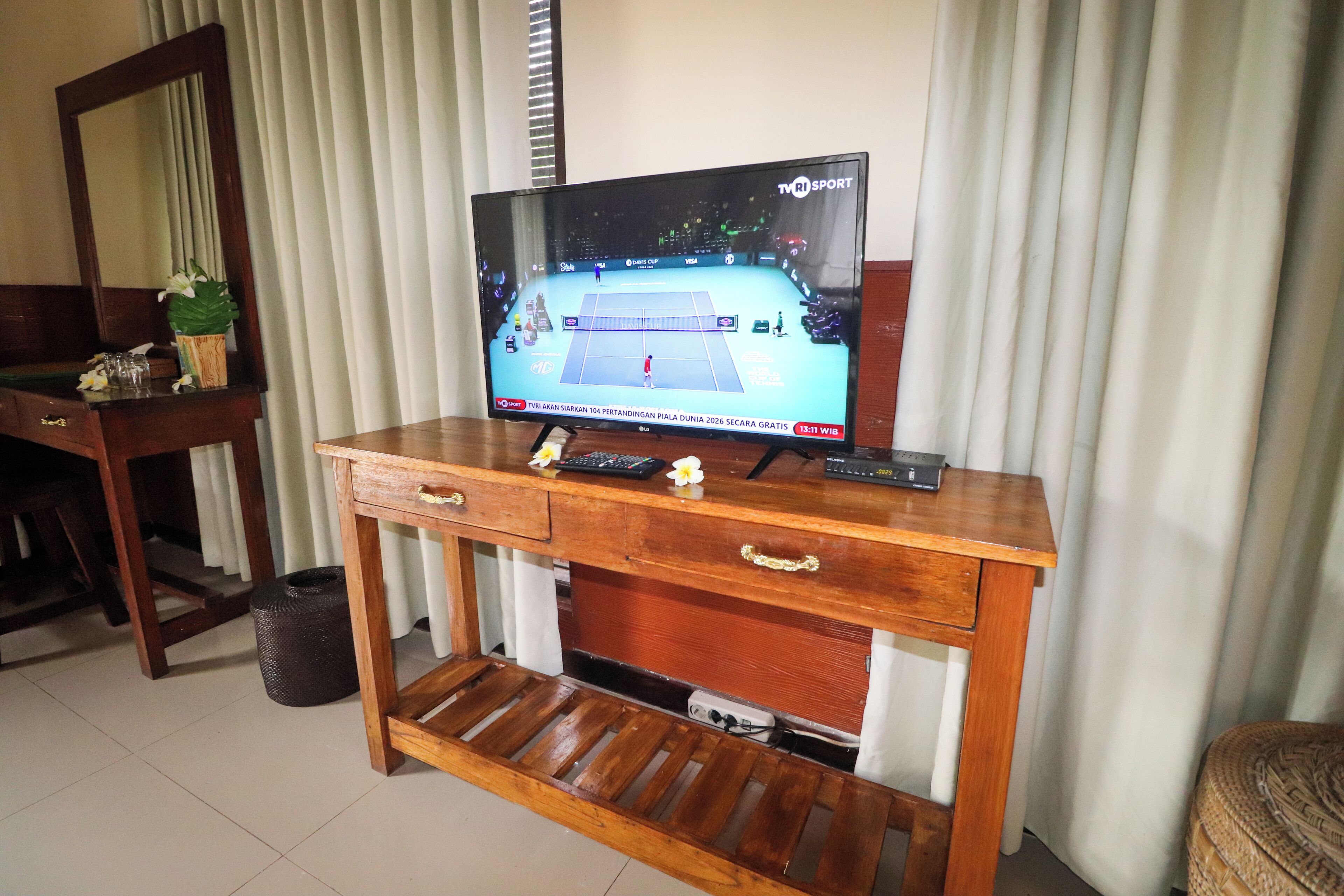 A wooden TV stand with a flat-screen TV displaying a sports event, a small plant, and a remote control.