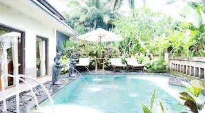 A swimming pool with a statue, lounge chairs, and lush greenery. - Villa JJ and Spa Ubud (Ubud)
