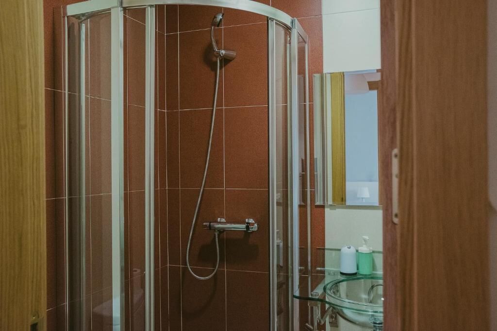 Une douche fermée par des parois en verre, dotée d’un pommeau de douche à main et d’un robinet mural.